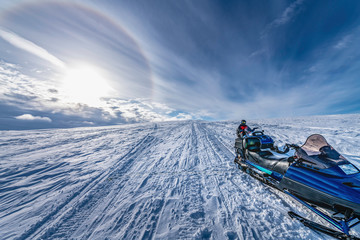 Two snowmobiles stand behind each other with a boy at second one. He dressed for driving in cold...
