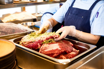The cook smears a large piece of beef with marinade for baking.