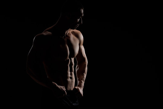 Muscular Model Sports Young Man In Jeans Showing His Press On A Black Background. Fashion Portrait Of Sporty Healthy Strong Muscle Guy. Sexy Torso.