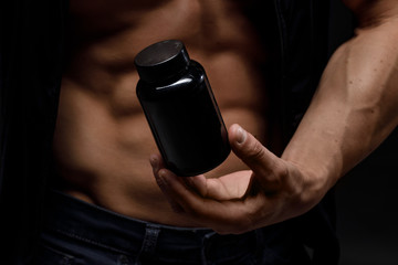 Model sports young man on dark background. Portrait of sporty strong muscle guy with protein drink in shaker. Sexy torso. Bodybuilding nutrition supplements, sport, workout, healthy lifestyle concept.