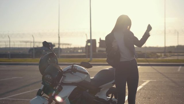 Beautiful young red-haired woman motorcyclist dancing next to her custom bike with black motorcycle helmet