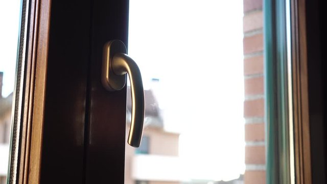 The man holding the Golden handle closes the brown plastic window. Outside the house against the bright sky