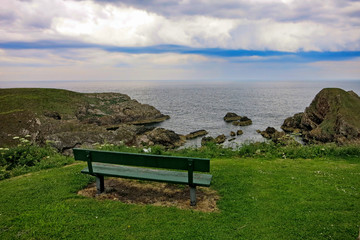 Naklejka na ściany i meble Coastal trail Buckie Scotland cliffs and rocks in the ocean view with a bench 