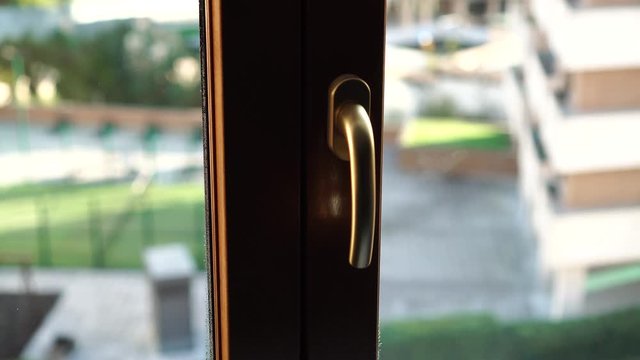 A fabric white mesh curtain of blinds rises and opens a brown plastic window. Outside a beautiful courtyard with houses and vegetation