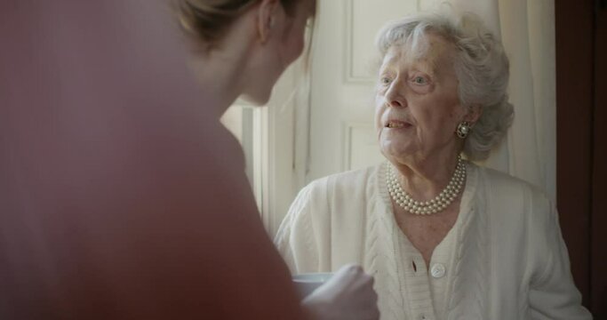 Multigeneration women talking together. Senior grandma woman smiling with her granddaughter visiting near window drinking tea or coffee.White hair elderly grandmother at home.4k slow motion