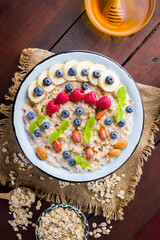 Bowl of oatmeal porridge with berries, honey and fruits on burlap. Tasty oatmeal with raspberries, blueberries and nuts on wooden boards. Healthy breakfast