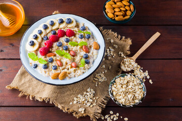 Bowl of oatmeal porridge with berries, honey and fruits on burlap. Tasty oatmeal with raspberries, blueberries and nuts on wooden boards. Healthy breakfast