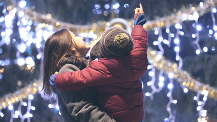 Portrait of mother holding child in her arms and admiring Christmas tree outdoor