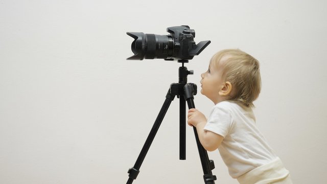 Funny baby child looking on photo camera scree on tripod, determined to work
