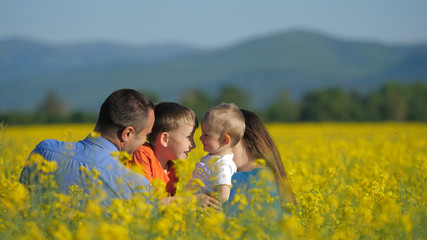 Fototapeta premium Happy family in blossom rape field, children play, kiss and embrace, smiling