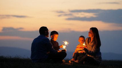 Parents and children silhouettes holding fireworks, sunset sky, celebration