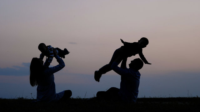 Mother And Father Silhouettes Lifting Up Baby And Brother To Sunset Sky, Parents