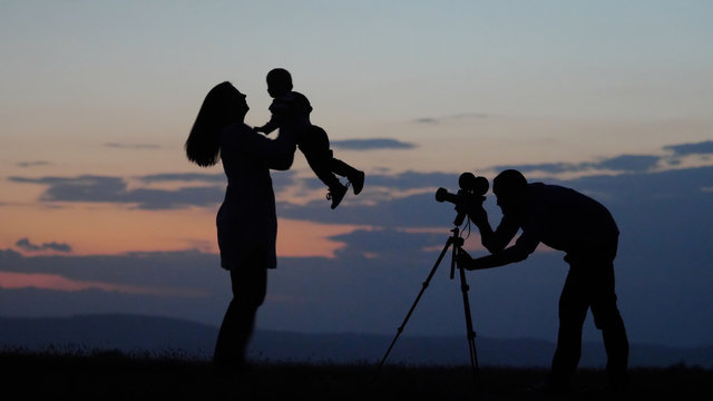 Mother with baby silhouettes dancing close sunset sky, father take pictures