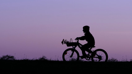 Child silhouette riding bike on hill close sunset sky, isolated kid in nature