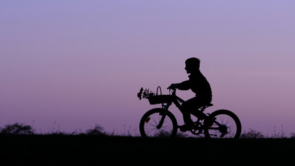 Obraz premium Child silhouette riding bike on hill close sunset sky, isolated kid in nature