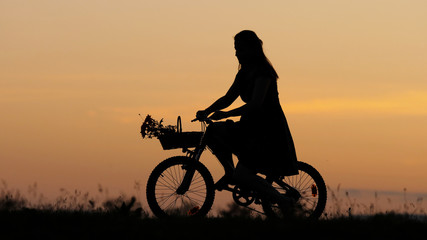Fototapeta na wymiar Young woman silhouette arrange flowers bouquet on bike basket, girl ride, sunset
