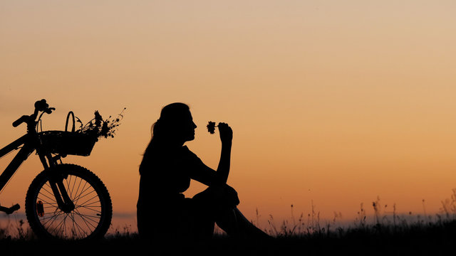 Isolated young woman silhouette sit close bike on hill, copy space