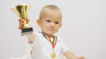 Portrait of baby child rising up golden cup, kid offering his victory trophy