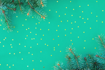 Fototapeta na wymiar Christmas composition with borders of fluffy green fir branches and golden confetti stars sparse on trendy mint background. Top view, flat lay style, copy space for text.
