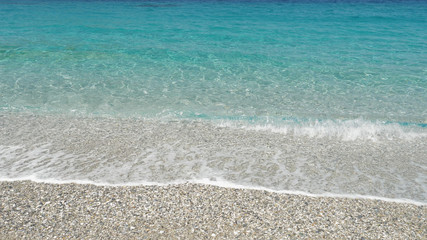 Fototapeta na wymiar Crystal clear turquoise shallow sea water waves washing the beach