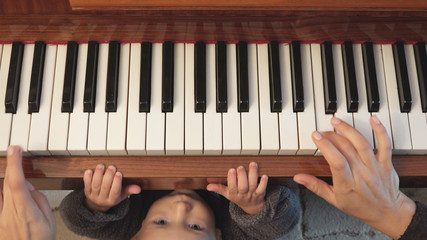 Detail of parent hands and funny little child playing at piano