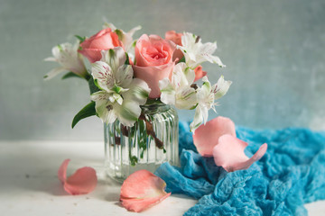 Peach Roses and White Alstroemeria arranged in a clear vase; White Table, Blue Accent Cloth; Neutral Background