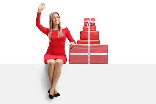 Young woman in a red dress sitting on a banner with presents and waving