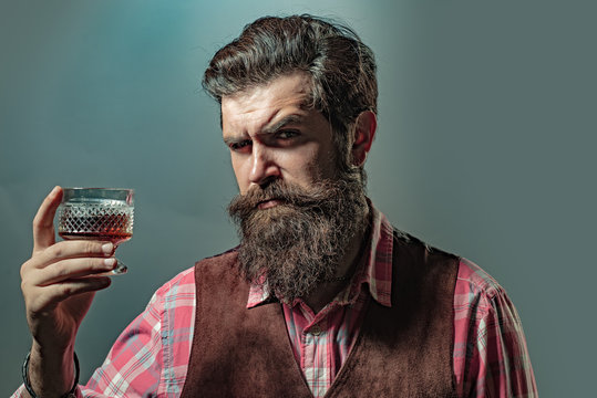 Hipster with beard and mustache in suit drinks alcohol after working day. Man or businessman drinks whiskey on black background.