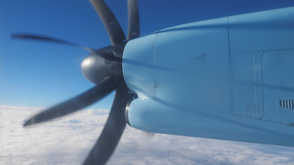 Detail of spinning propeller on plane wing, flying over white fluffy sky on sky