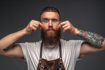 Stylish tattooed hairdresser grimacing at camera touching face