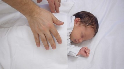 Caring mother hand covering the newborn baby with a blanked for sleep