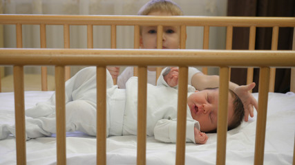 Mother and baby brother looking at newborn sleeping in a child crib