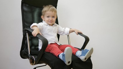 Little child sitting and spinning in a business chair, funny kid smiling
