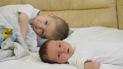Portrait of toddler lie next by newborn baby brother, resting on bed close