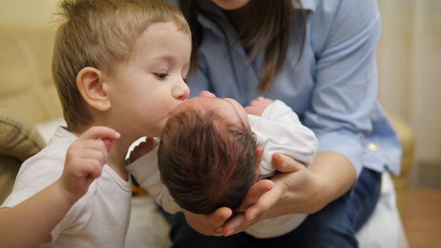 Focus on newborn in mother arms, brother give a kiss to baby