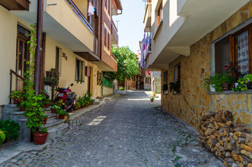 European narrow cobble-paved street between classic houses in the old town. Small passage between brick buildings with windows. Plants and flowers in pots near walls. Linen dries on rope in street