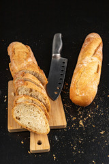 Pieces of fresh baguette and a knife on a wooden board. Delicious bread prepared to make sandwiches.