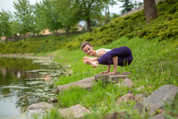 Fototapeta na wymiar A young sports girl practices yoga on a green lawn by the river, yoga assans posture. Meditation and unity with nature
