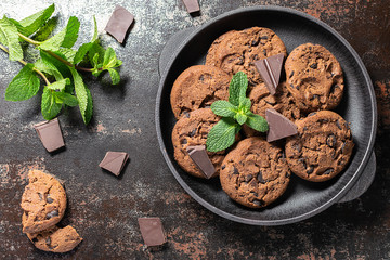 Fresh homemade chocolate cookies with chocolate pieces and mint leaves on black vintage table. Tasty homemade dessert concept.