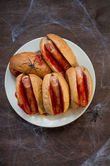 Halloween food. Halloween hot dog. Bloody fingers from sausages in rolls with ketchup. Scary food. Themed food. Dark wooden background.