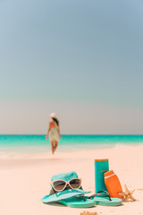 Fototapeta na wymiar Suncream bottles, sunglasses, flip flop on white sand background ocean