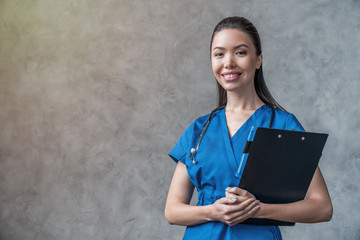 Young asian doctor woman with stethoscope and folder in hands isolated on gray background