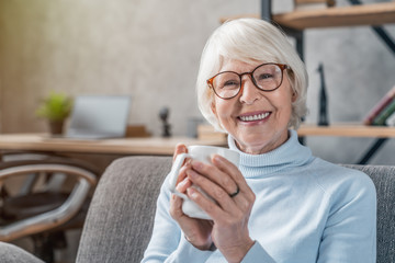 Senior woman drinking hot drink sitting on sofa at home