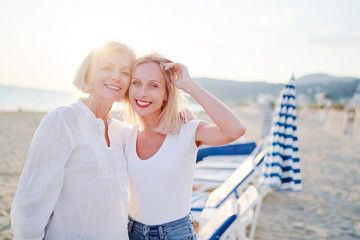 Fototapeta na wymiar Outdoor portrait of smiling happy caucasian senior mother with her adult daughter hugging and looking at the camera on sea beach.