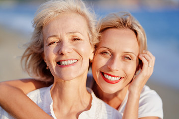 Outdoor close up portrait of smiling happy caucasian senior mother with her adult daughter hugging...
