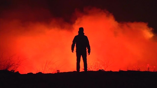 Silhouette shot, moving towards a man standing in front of burning nature, looking at the damage of the Californian wildfires, at night time, in Northridge, Los Angeles, California, USA