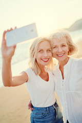 Outdoor portrait of smiling happy caucasian senior mother with her adult daughter taking selfie on...