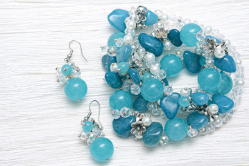 Blue earrings and necklace bijouterie on white wooden table background.