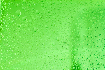 Raindrops on the surface of window panes. Natural pattern of raindrops, with green highlights on a blue background.