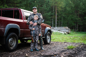 Happy hunter with his son near their pickup truck before hunting in a forest - obrazy, fototapety, plakaty